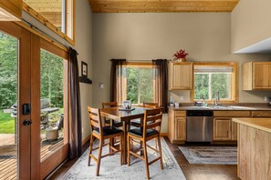 Une cuisine avec des meubles en bois, une table à manger avec des chaises et de grandes fenêtres.