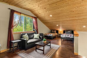 A loft-style room with a sloped ceiling, a sofa, a coffee table, and two beds with patterned bedding. - Nature's Acres | Private Hot Tub, Pond & Gazebo (Leavenworth)
