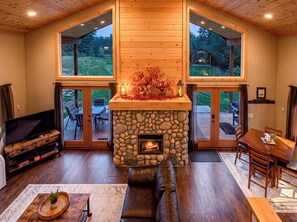 A spacious living room with a stone fireplace, large windows, and a cozy seating area. - Nature's Acres | Private Hot Tub, Pond & Gazebo (Leavenworth)