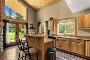 A modern kitchen with wooden cabinets, a bar area, and large windows. - Nature's Acres | Private Hot Tub, Pond & Gazebo (Leavenworth)