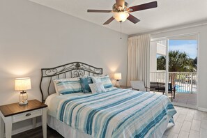 A bedroom with a bed, nightstands, a ceiling fan, and a view of a pool through a sliding glass door. - Destin West Gulfside 212 ~ Gulf & Pool Views! (Fort Walton Beach)