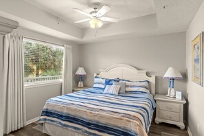 A bedroom with a bed, two bedside tables, a ceiling fan, a window with curtains, and a painting on the wall. - Destin West Gulfside 203 ~ Ocean Views ~ Free Beach Service! (Fort Walton Beach)