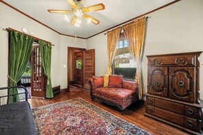 A room with a wooden floor, a patterned rug, a sofa, a cabinet, and a ceiling fan.
