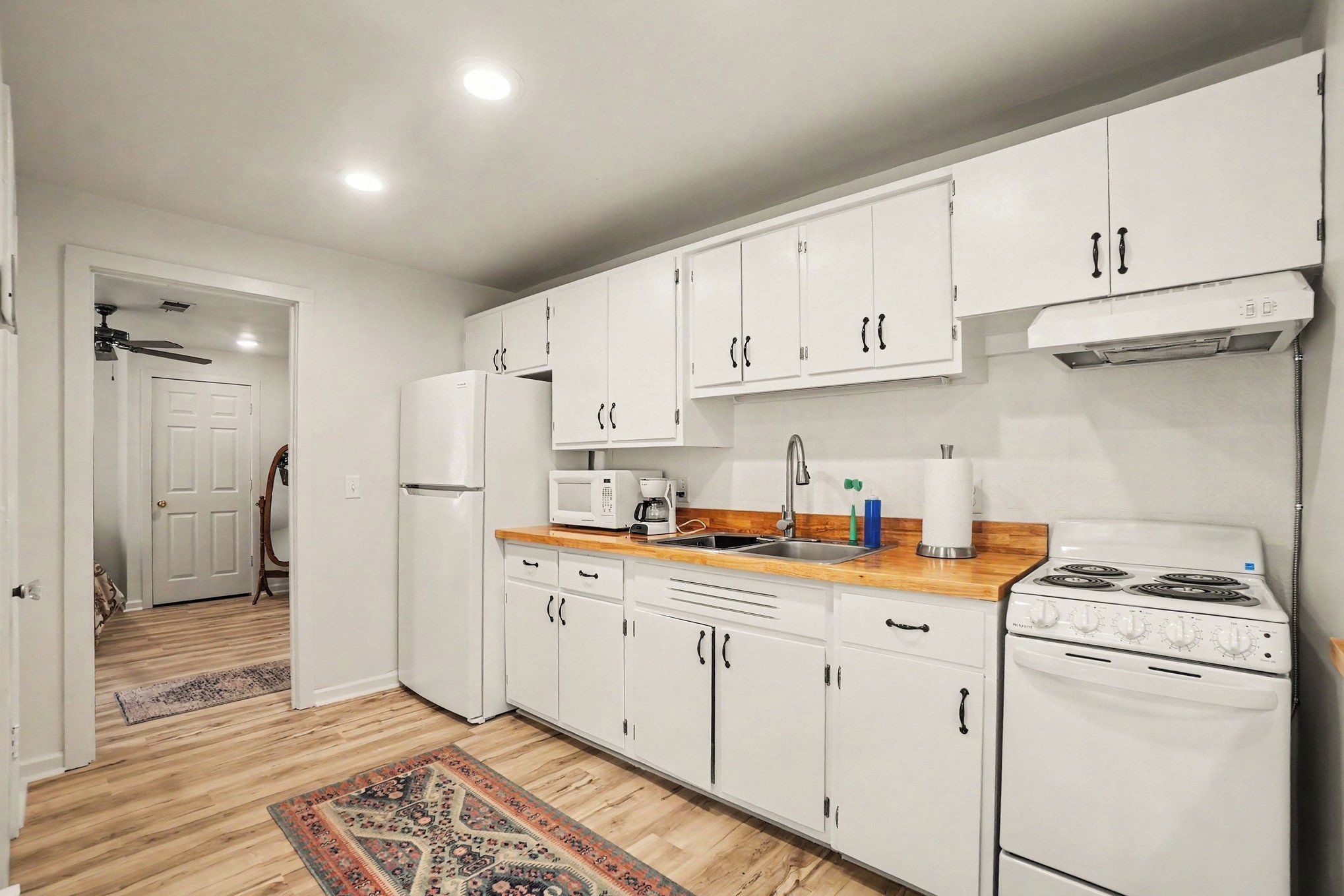 A modern kitchen with white cabinets, a stove, a microwave, and a refrigerator.