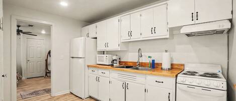 A modern kitchen with white cabinets, a stove, a microwave, and a refrigerator.