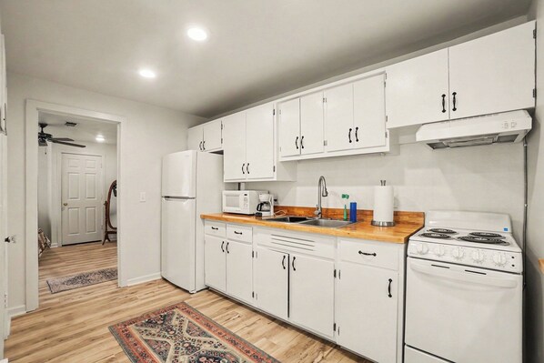 A modern kitchen with white cabinets, a stove, a microwave, and a refrigerator.