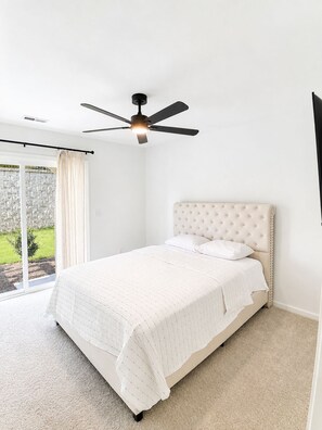 A bedroom with a bed, a ceiling fan, and a view of the outdoors. - Welcome to your modern luxury retreat, just 9 minutes from Downtown Raleigh! (Raleigh)