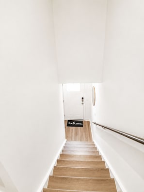 A staircase with a wooden finish, white walls, and a welcome mat at the bottom. - Welcome to your modern luxury retreat, just 9 minutes from Downtown Raleigh! (Raleigh)