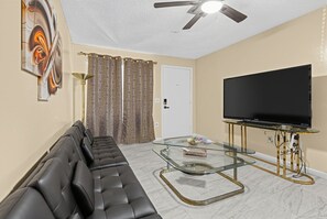 A living room with a sofa, a glass coffee table, a flat-screen TV, and a ceiling fan. - Central OKC Getaway | Bricktown, Zoo & Route 66 (Oklahoma City)