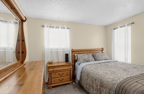 A bedroom with a wooden bed, a nightstand, a mirror, and a window with curtains. - Central OKC Getaway | Bricktown, Zoo & Route 66 (Oklahoma City)