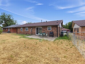 A single-story brick house with a patio, a barbecue grill, and a fenced yard. - Central OKC Getaway | Bricktown, Zoo & Route 66 (Oklahoma City)