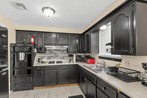 A modern kitchen with black cabinets, a stainless steel sink, and a built-in oven. - Central OKC Getaway | Bricktown, Zoo & Route 66 (Oklahoma City)