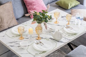 Ein Esstisch ist gedeckt mit Tellern, Gläsern, einer Kerze und einer Teekanne, umgeben von Kissen und einer Vase mit Blumen.