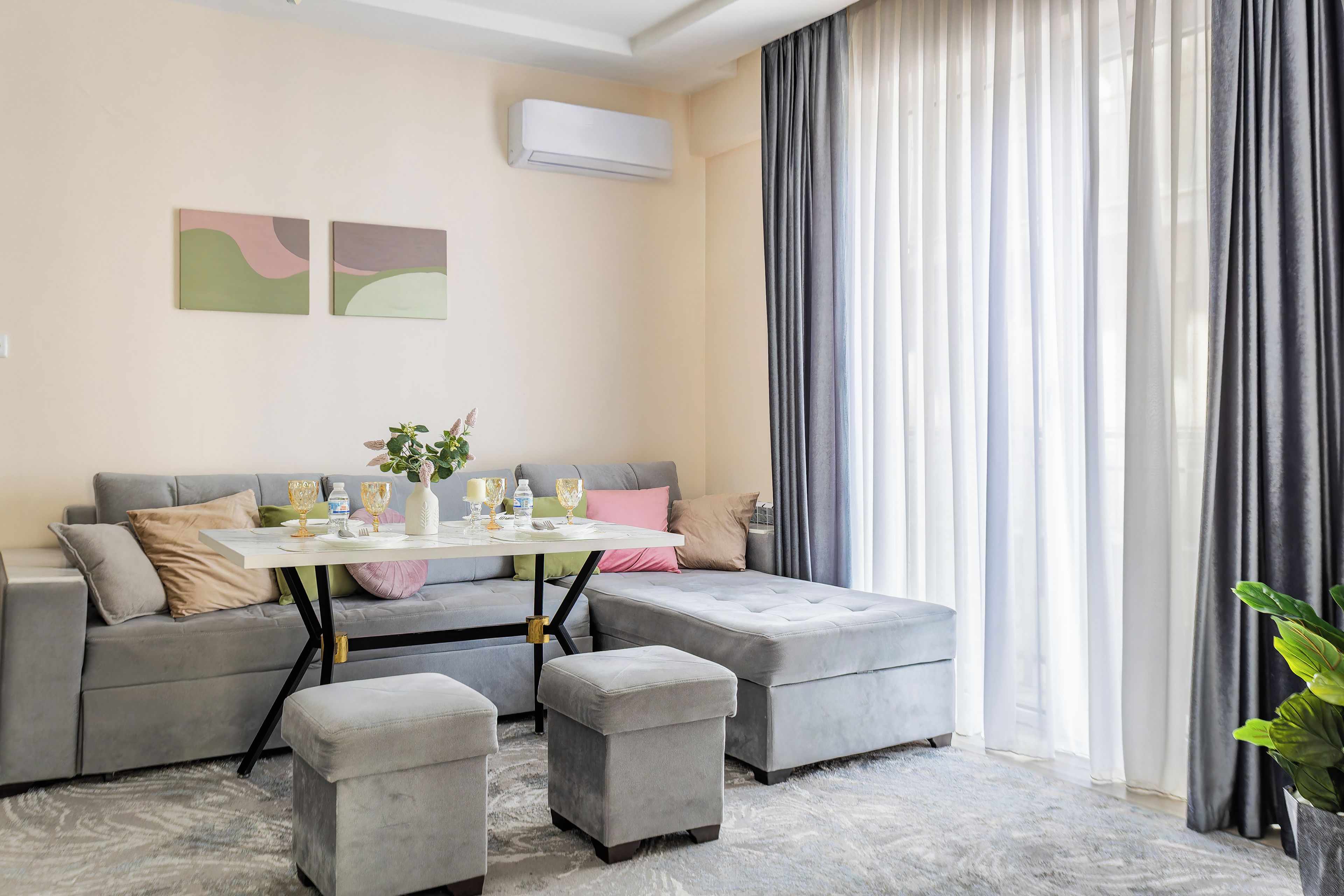 Una sala moderna con un sofá seccional gris, una pequeña mesa lista para comer y un ventanal con cortinas.