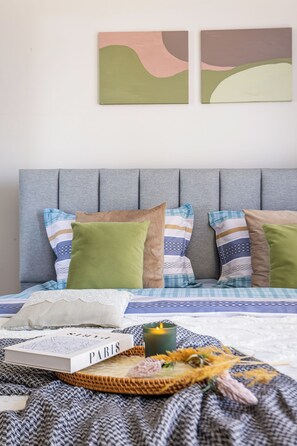 Cama bem arrumada com um livro intitulado 'PARIS', uma vela, um tabuleiro de tecido e elementos decorativos.