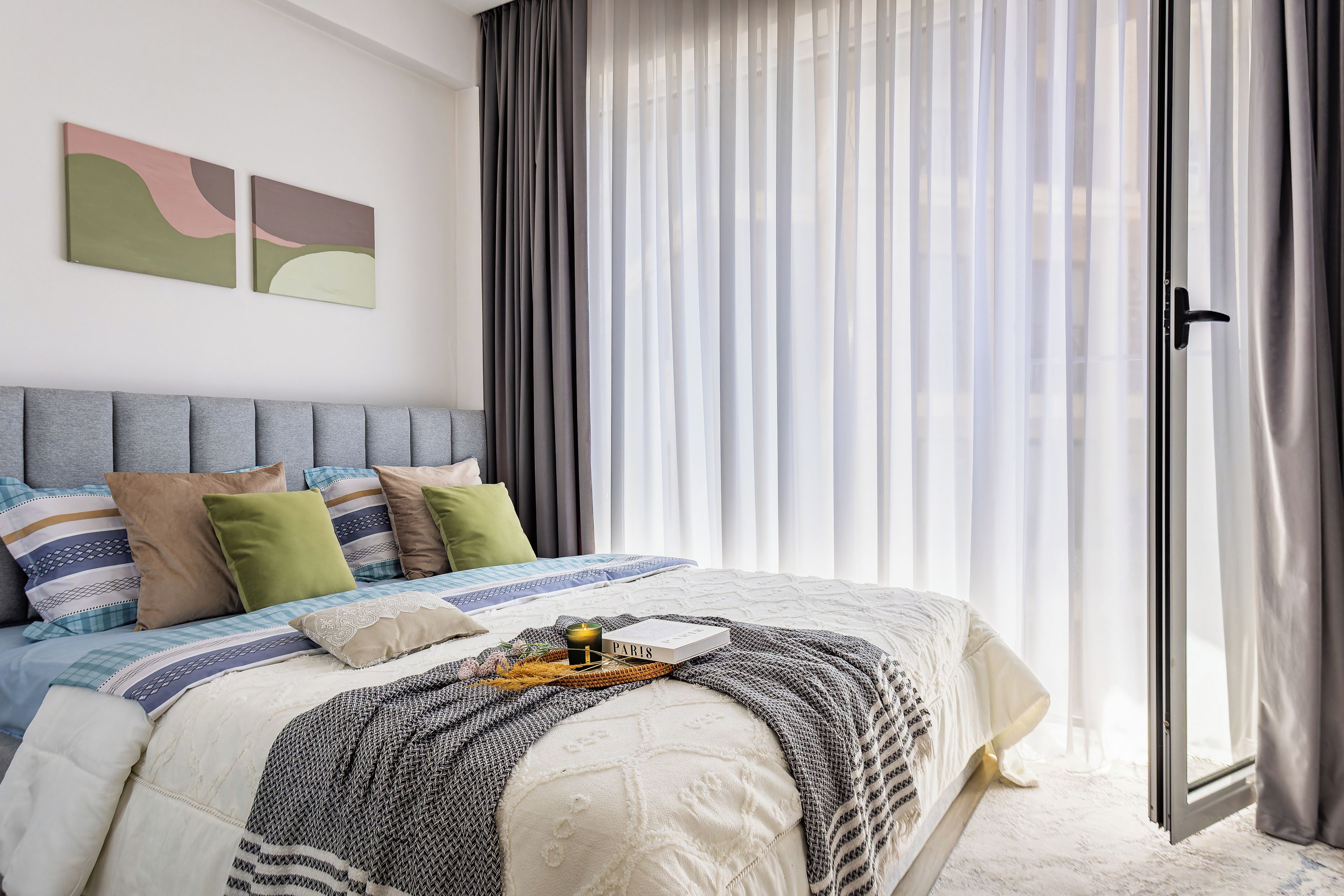 A modern bedroom with a bed, pillows, a bedside table, and a window with curtains.