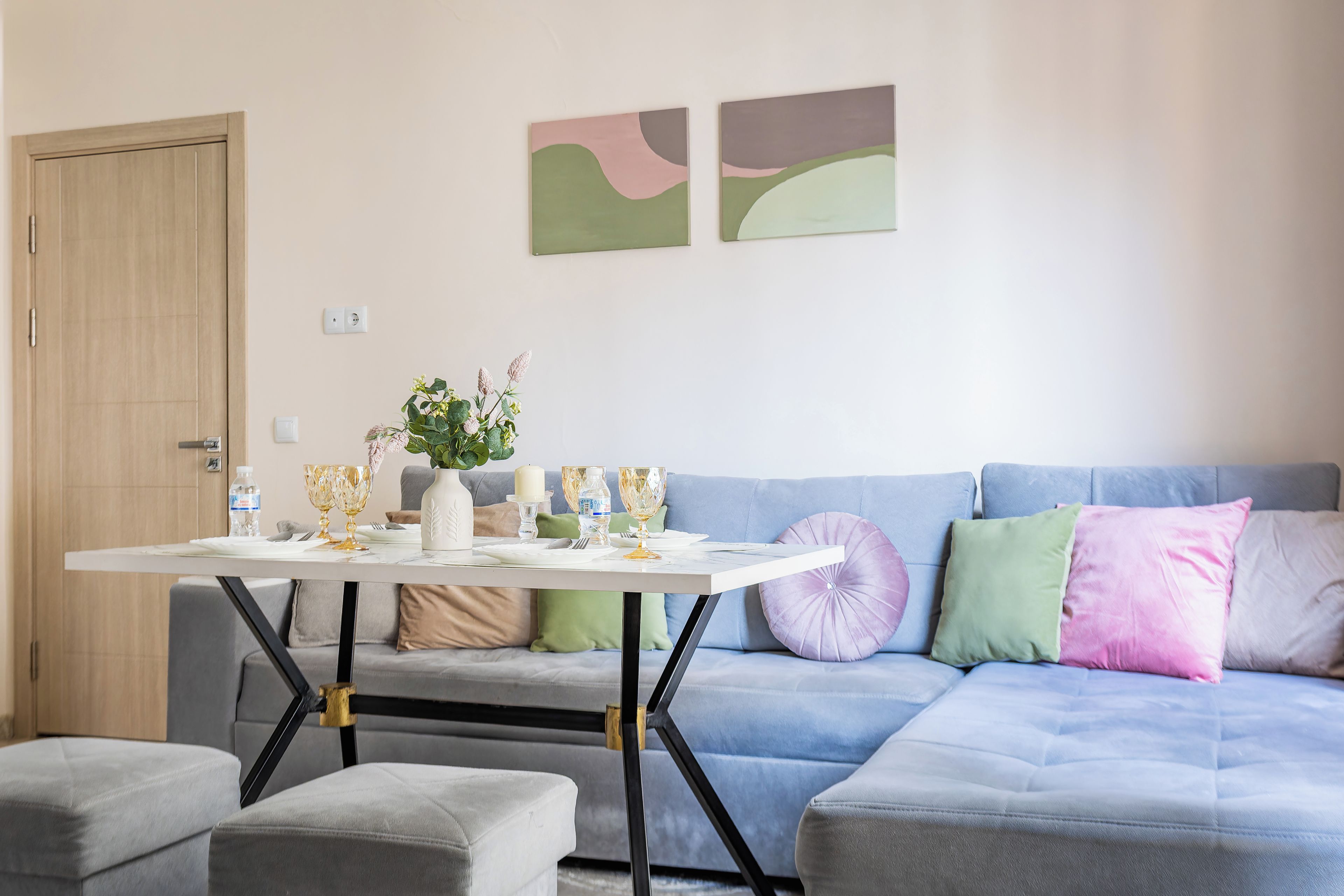 Una sala de estar moderna con una mesa de comedor preparada para dos personas, un sofá con almohadones de colores y arte abstracto en la pared.