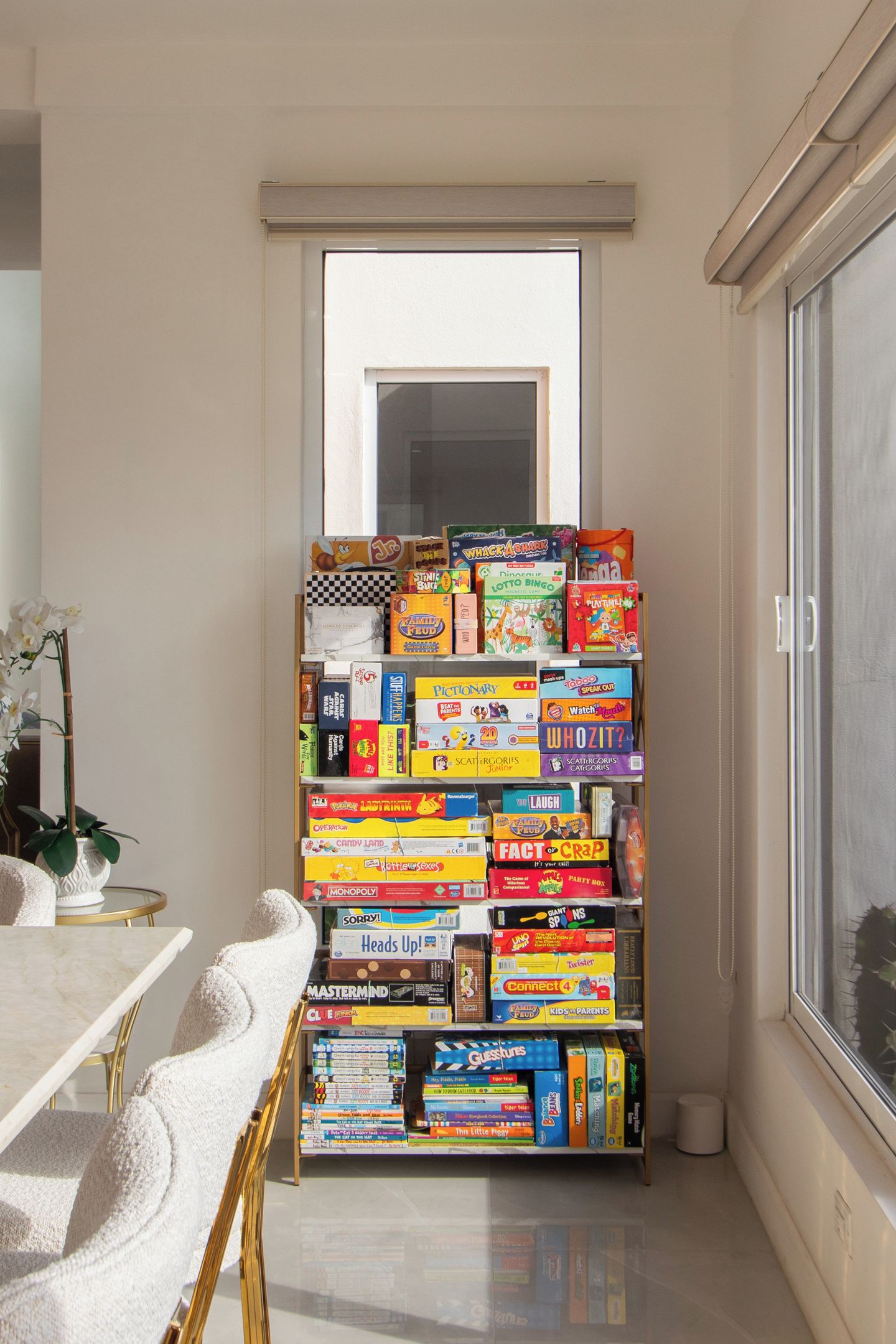 A room with a bookshelf filled with various board games, a window, and a potted plant.