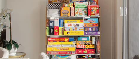 A room with a bookshelf filled with various board games, a window, and a potted plant.