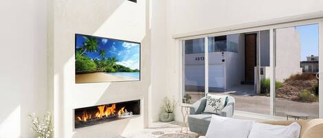 A modern living room with a fireplace, a large TV, and a view of the outside.