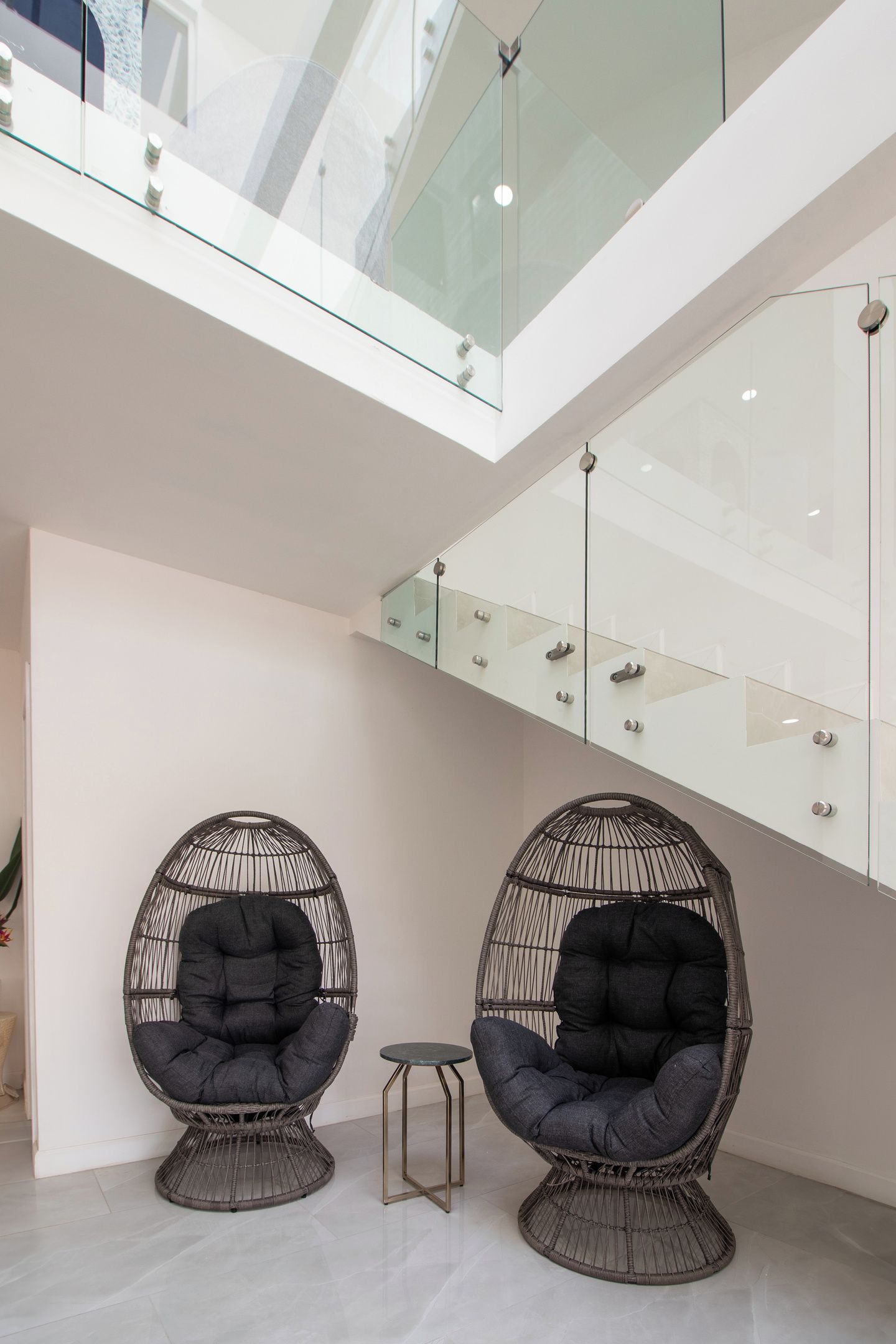 A modern interior with two wicker chairs, a small table, and a glass railing.