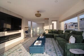 A modern living room with a large flat-screen TV, a sectional sofa, a blue ottoman, and a patterned rug. - Oceanview Villa | Rooftop Hot tub, Sauna, Fire Pit (Rosarito)