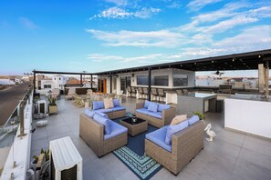 Eine Dachterrasse mit Korbmöbeln, einer Bar und Blick auf die Stadtlandschaft.