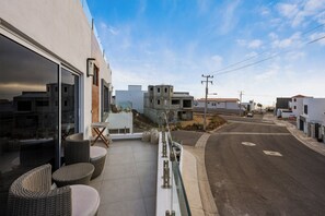 A residential area with modern buildings, a paved street, and outdoor seating with wicker furniture. - Oceanview Villa | Rooftop Hot tub, Sauna, Fire Pit (Rosarito)