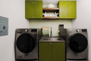 A compact laundry area with two front-loading washing machines, a sink, and green cabinetry. - Oceanview Villa | Rooftop Hot tub, Sauna, Fire Pit (Rosarito)
