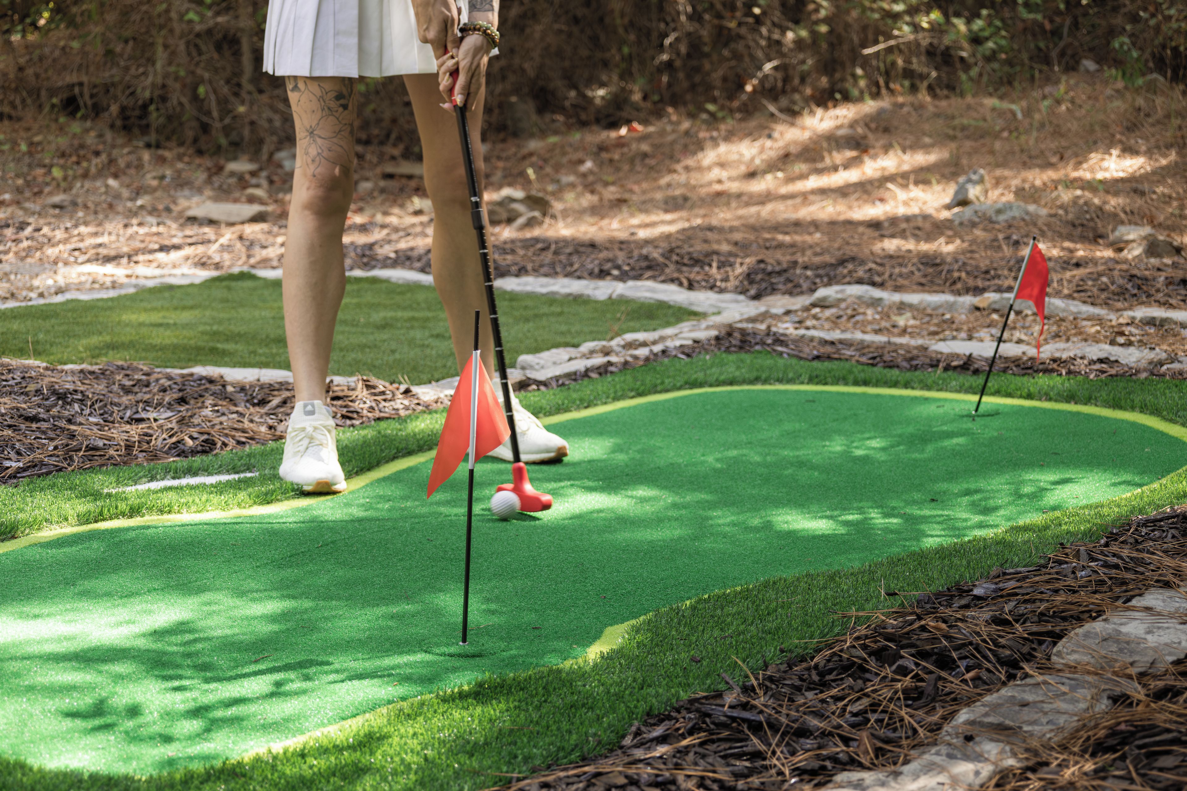 A person playing golf on a green with a flagstick and a golf ball.