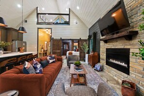 A modern living room with a fireplace, a sofa, a coffee table, and a television mounted on the wall. - Luxe Couples Cabin: Outdoor Cinema+Stargaze Net+Sauna+Plunge+MiniGolf (Broken Bow)