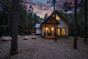 Eine Holzhütte mit großen Fenstern und einem Schotterweg, umgeben von Bäumen.