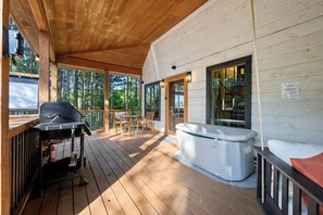 Eine Holzterrasse mit Whirlpool, Grill und Blick ins Waldgebiet.
