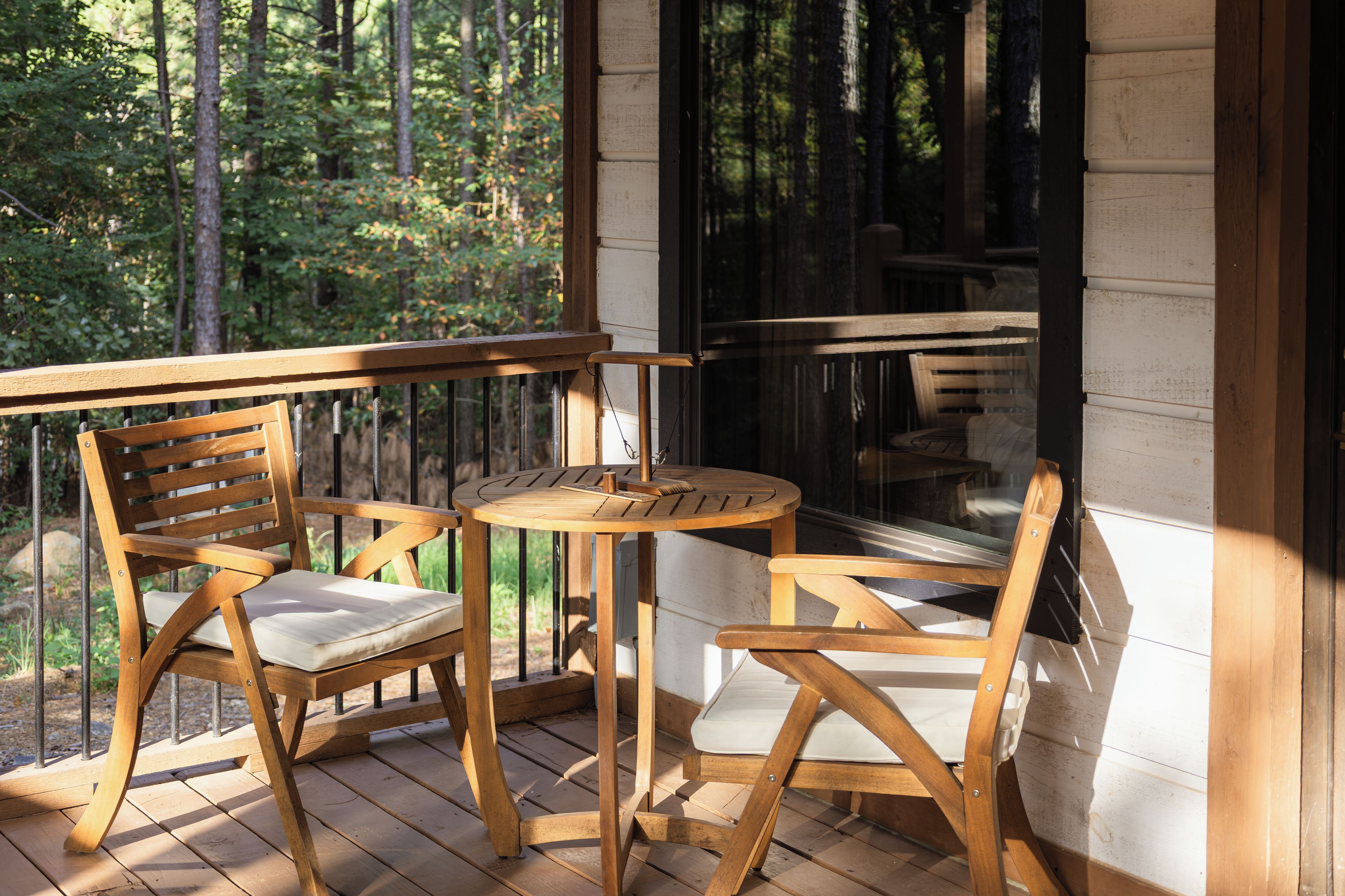 Una terraza de madera con dos sillas y una mesa, con vistas a una zona boscosa.