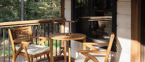 Una terraza de madera con dos sillas y una mesa, con vistas a una zona boscosa.