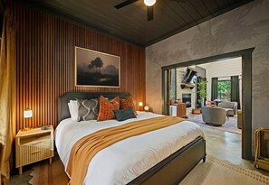 Ein modernes Schlafzimmer mit einem großen Bett, Holzvertäfelung, einem Gemälde und Blick in einen angrenzenden Raum.