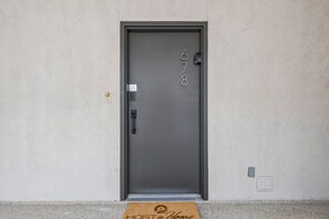 Een deur met een numeriek keypad, een kaartlezer en een deurmat met de tekst 'HOST & Home'.