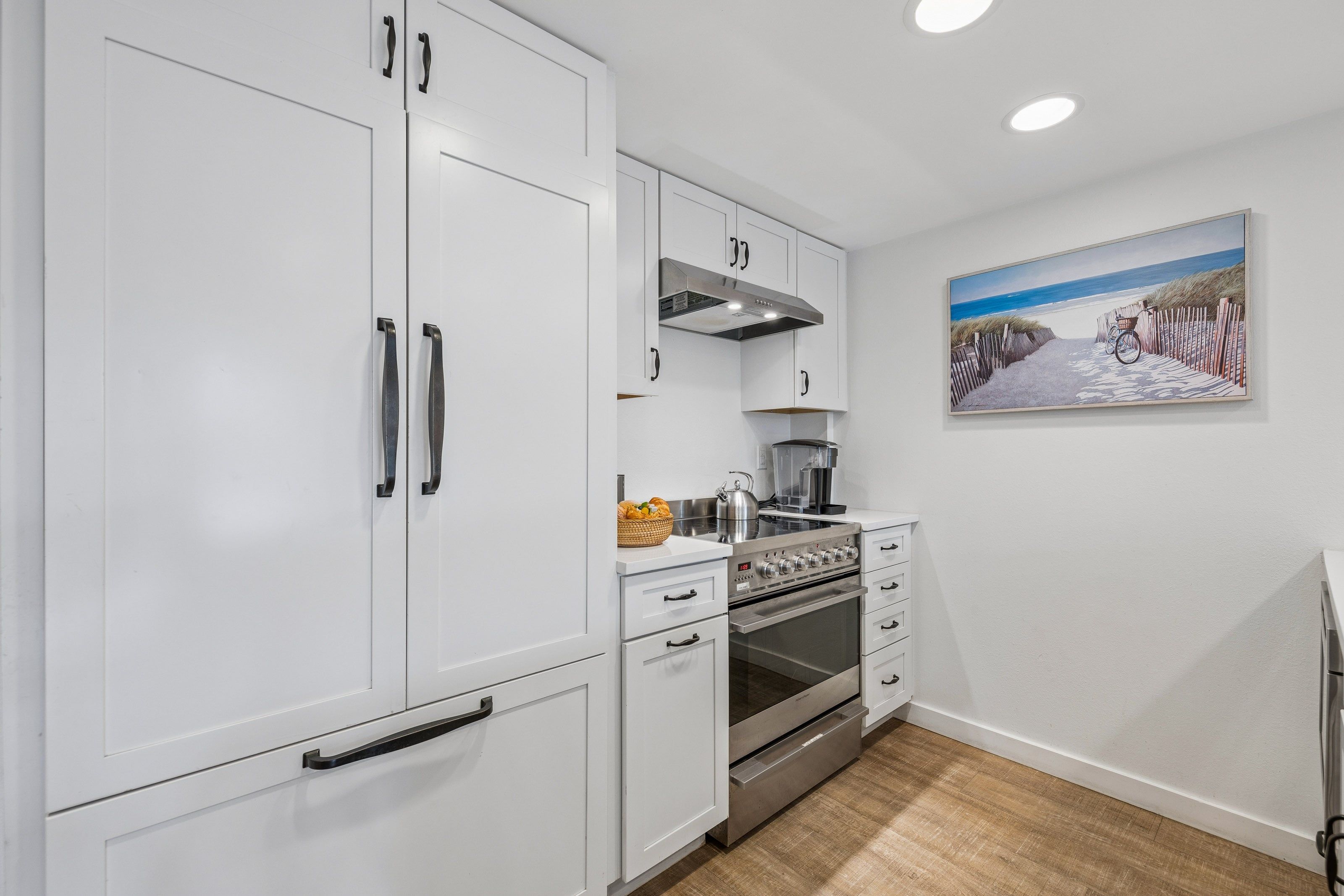 A modern kitchen with white cabinetry, a stainless steel oven, and a painting of a beach scene.