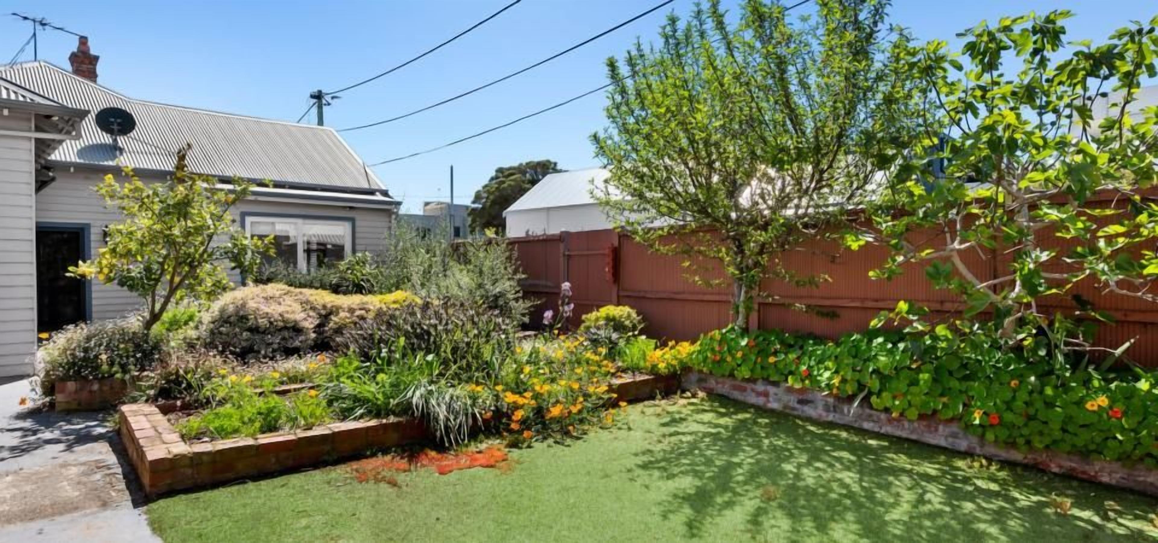 A residential garden with a lawn, various plants, and a brick border.