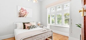 A bedroom with a bed, a bedside table, a window with blinds, and a door.