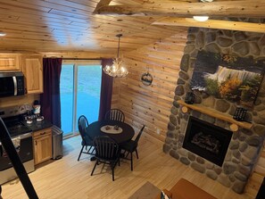 A cozy cabin interior with a stone fireplace, wooden ceiling, and a dining area with chairs and a table.