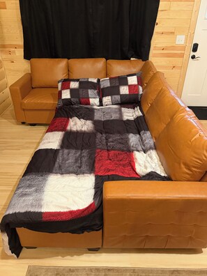 Un letto con una coperta a quadri, due divani in pelle marrone e una tenda nera.