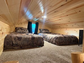 A cabin bedroom with two beds, a ceiling fan, and a window with curtains.
