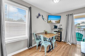 Ein Essbereich mit Holztisch und Stühlen, einem Fernseher an der Wand und Blick ins Freie.
