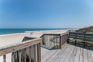 Ein Holzsteg führt zu einem Sandstrand, im Hintergrund das Meer.