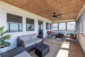 A covered outdoor area with a sofa, chairs, a table, and a ceiling fan. - The Bay House - Soundfront, Dock, Gazebo, Close to Beach, Shops, Restaurants, Flex Stays (Kill Devil Hills)