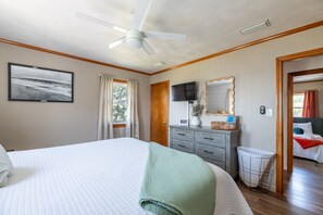 A bedroom with a bed, a dresser, a mirror, a television, and a ceiling fan. - The Bay House - Soundfront, Dock, Gazebo, Close to Beach, Shops, Restaurants, Flex Stays (Kill Devil Hills)