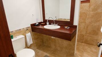 A bathroom with a wooden ceiling, a white toilet, a sink with a mirror above it, and beige tiled flooring.