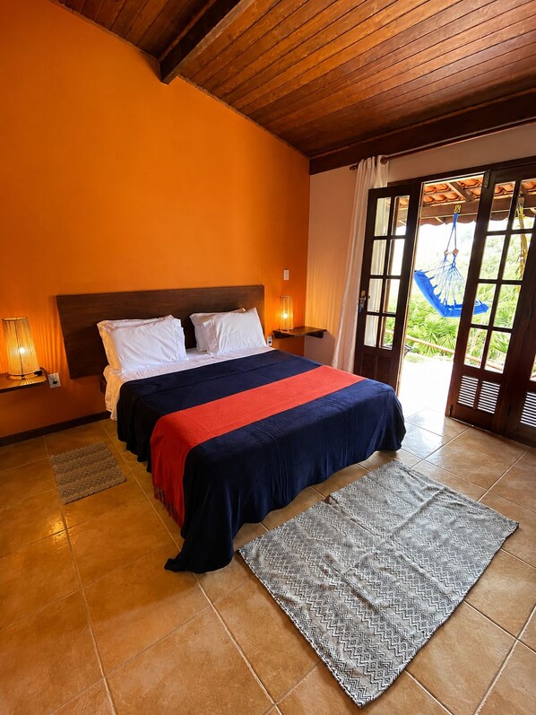 A bedroom with a bed, nightstands, a hammock, and a view through a glass door.