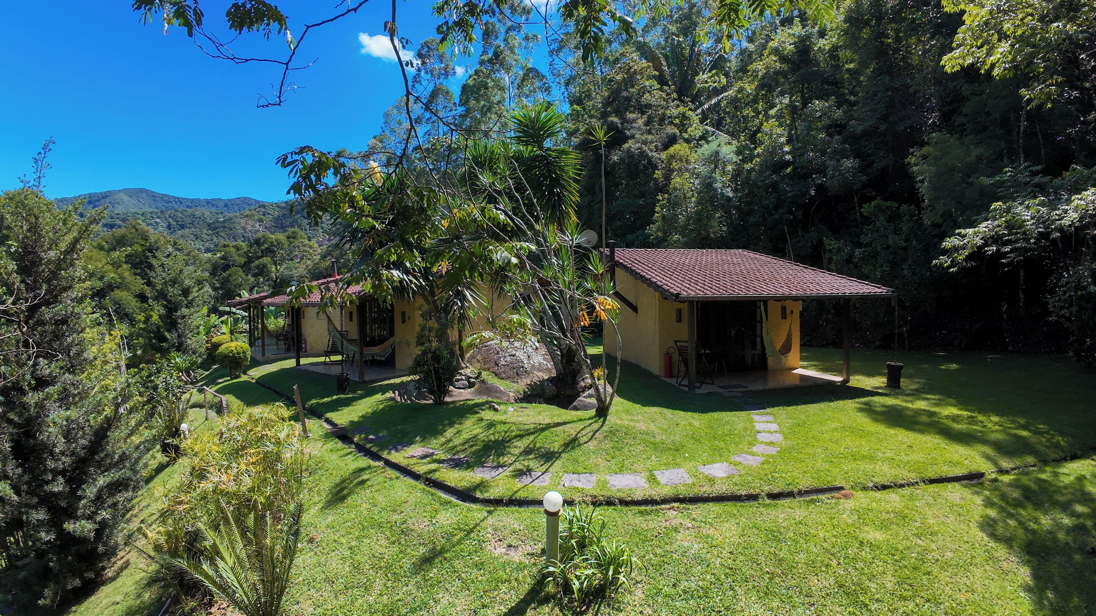 A two-story house with a red-tiled roof, surrounded by lush greenery and a clear blue sky.